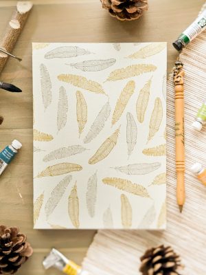 Photo du carnet "Plume de lumière" de la collection de carnets Les Confidents "Douce nuit". Couverture blanche avec des plumes dorées.