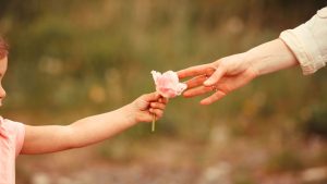 Photo avec la main d'une enfant qui tend une fleur à sa maman. Couverture de l'article "Idées cadeaux pour la fête des mères".
